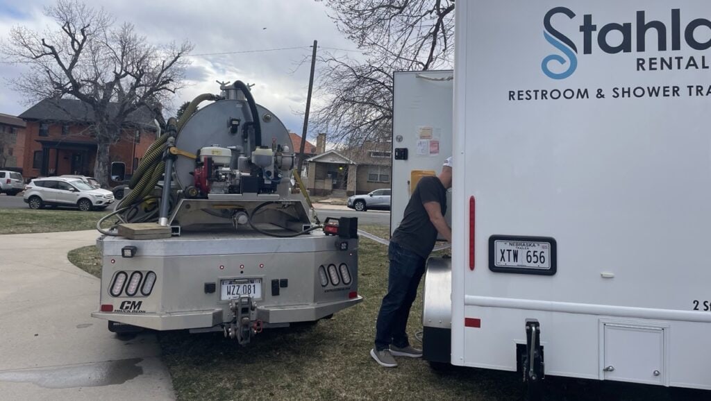 Man servicing portable restroom trailer on urban street.