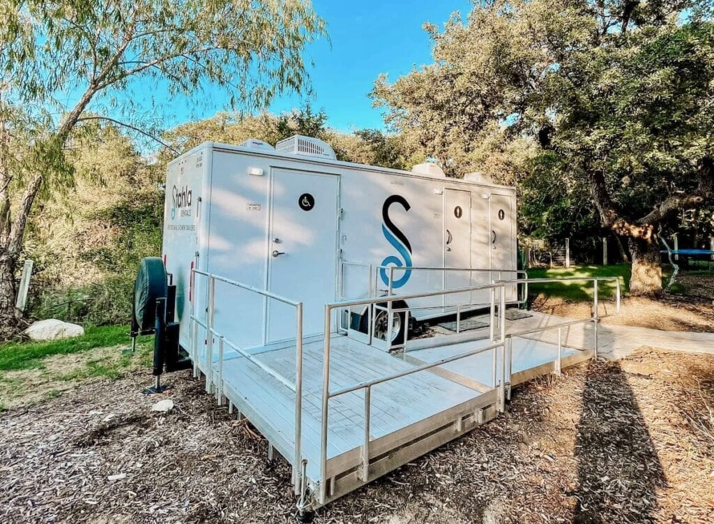 ADA Bathroom Trailer parked in a natural setting with trees in the background.