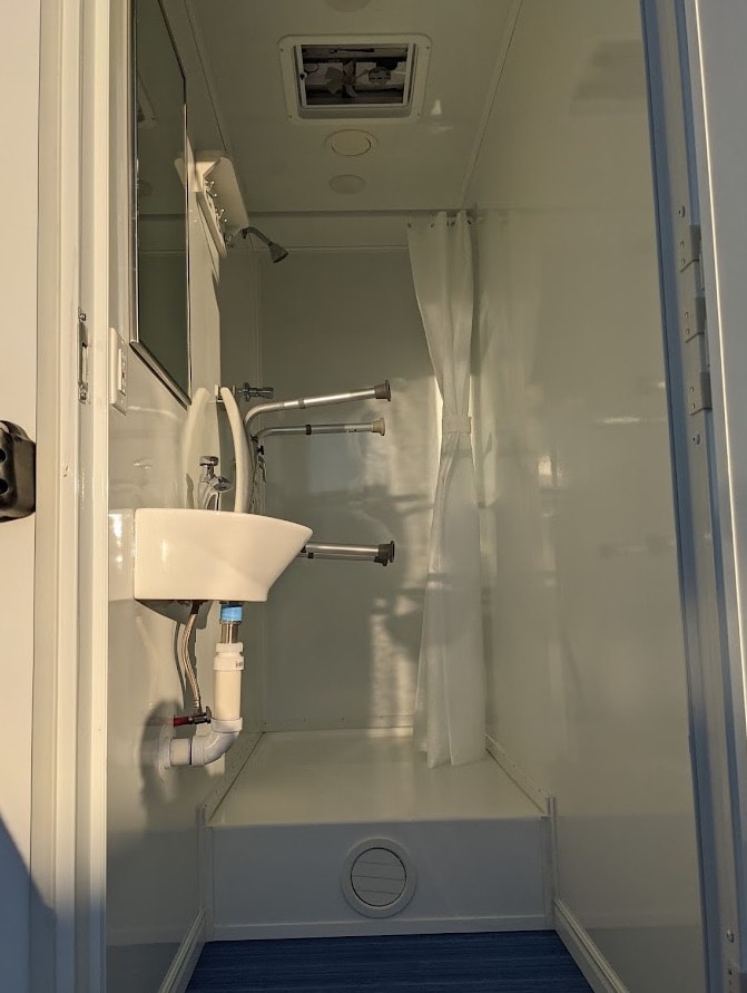 Compact bathroom with shower, sink, and white curtain.