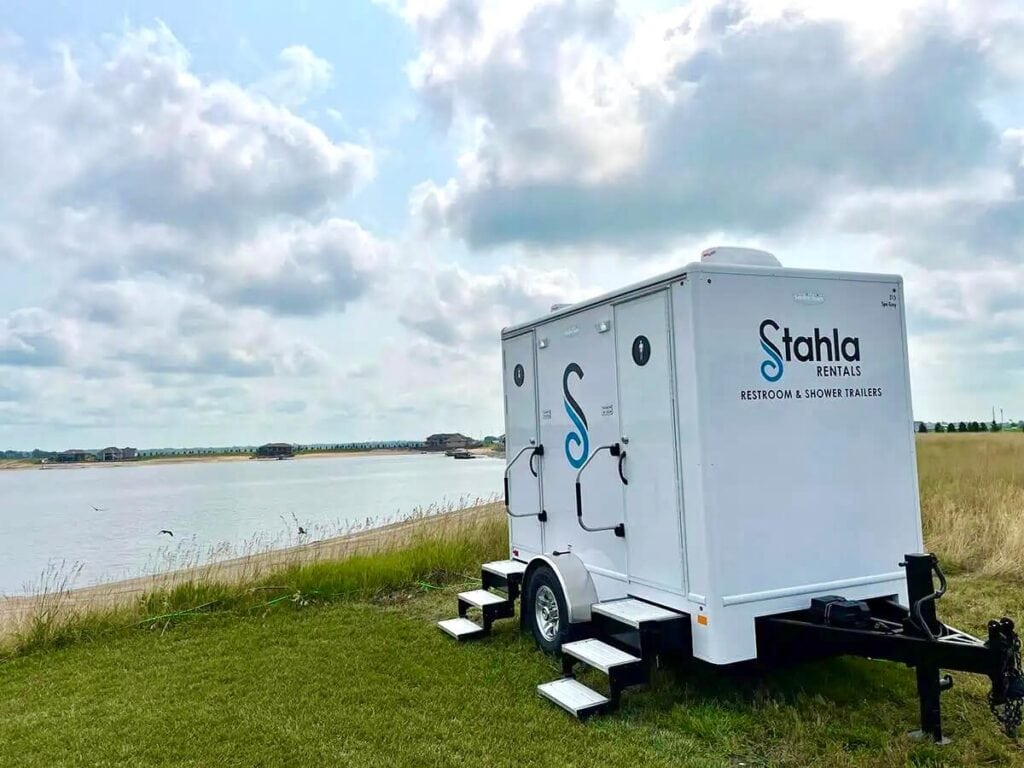 Mobile 2 Stall restroom trailer by lake with cloudy skies.