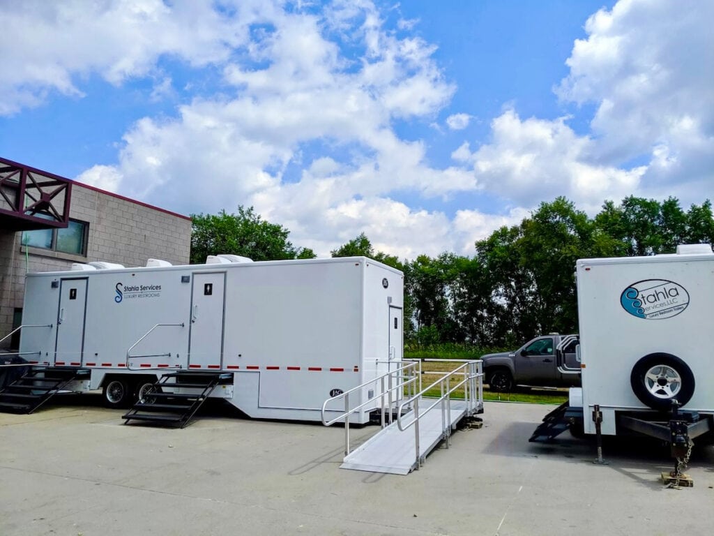 Mobile restroom trailers parked outdoors with clouds.
