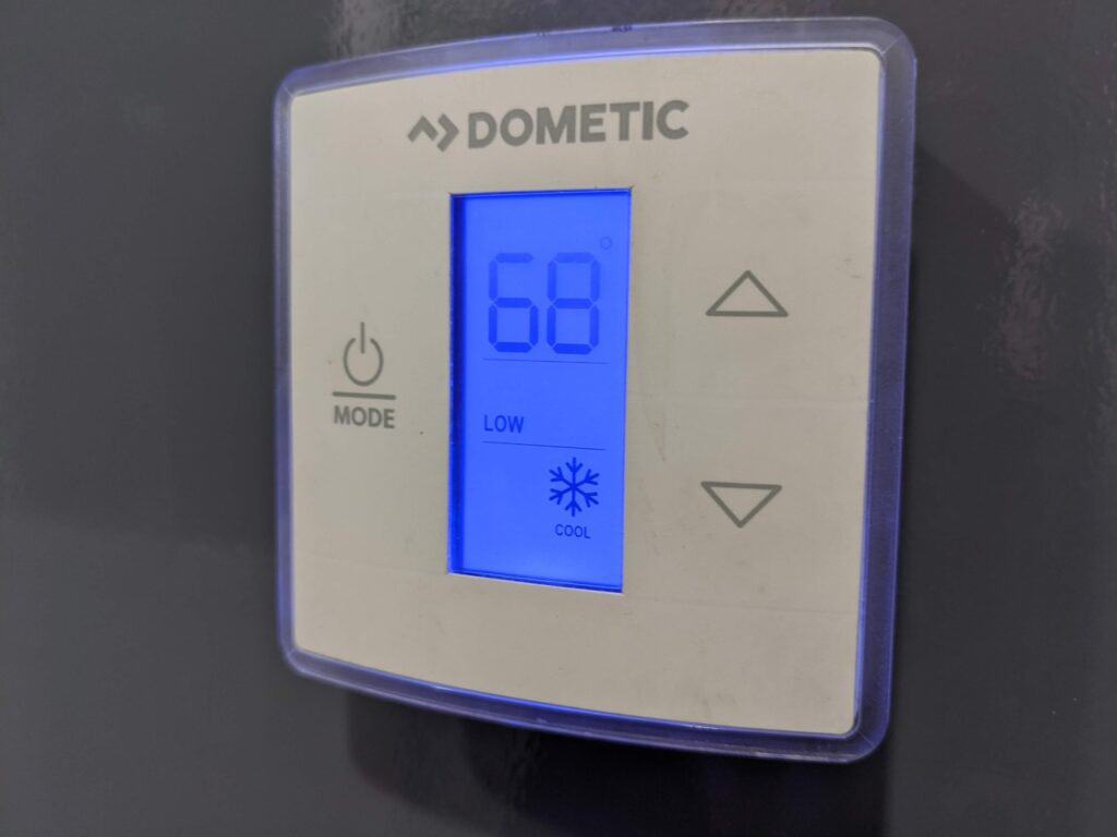 digital thermostat displaying a temperature of 68 degrees fahrenheit on a blue screen, set to 'cool' mode with a low fan speed in a 2 stall restroom trailer rental.