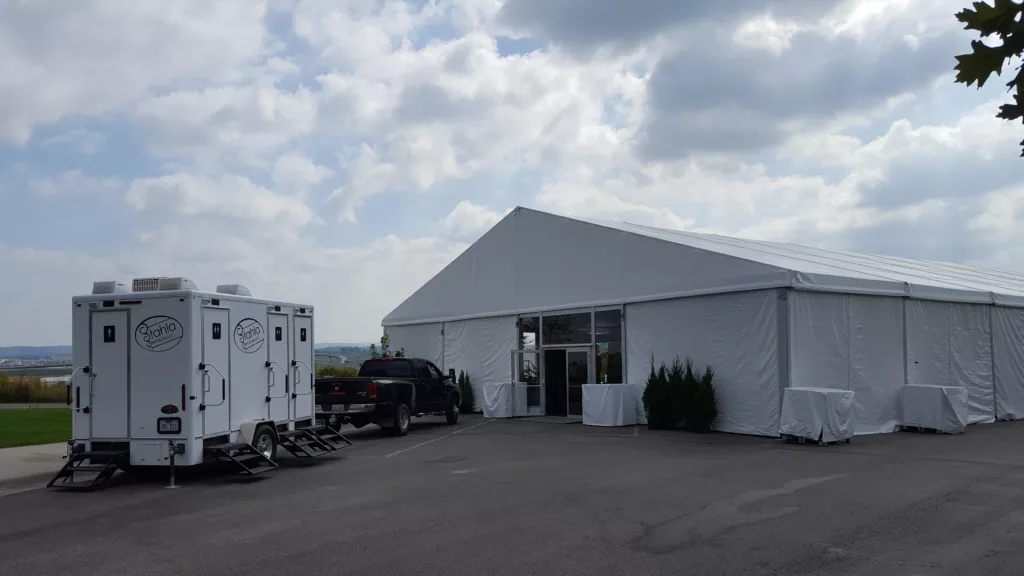 Large event tent with portable restroom trailer nearby.