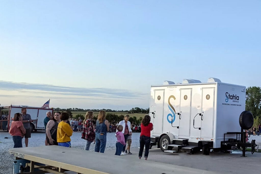 Outdoor event with portable 6 Stall restroom Trailers and gathering people.