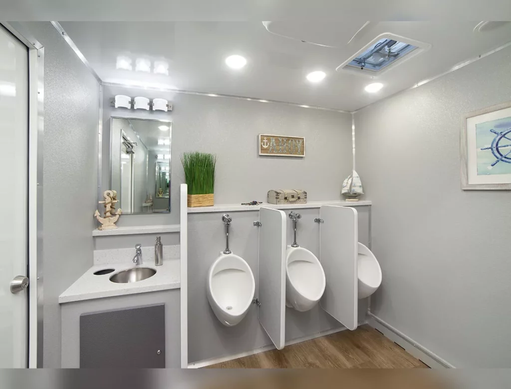 modern 10 stall restroom trailer for men, featuring three urinals and a sink, decorated with neutral tones and complete with a mirror and wall art.