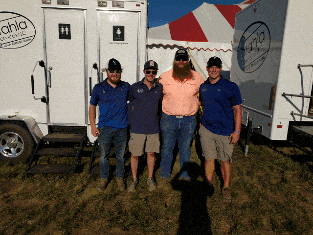 Four men smiling in front of event trailer.
