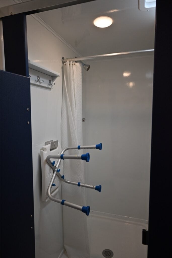 accessible shower cabin with a white curtain, grab bars, and blue support handles inside a modern bathroom featuring an 8 station shower.