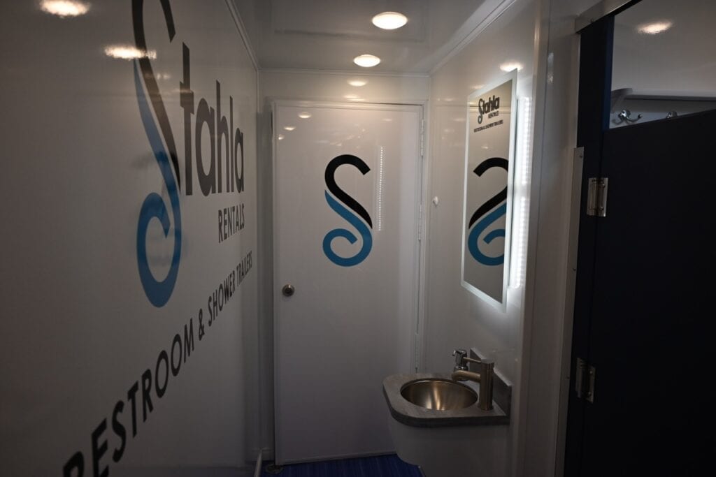 interior of a mobile shower unit featuring a sink and doors marked with male and female symbols on a blue and white themed wall.