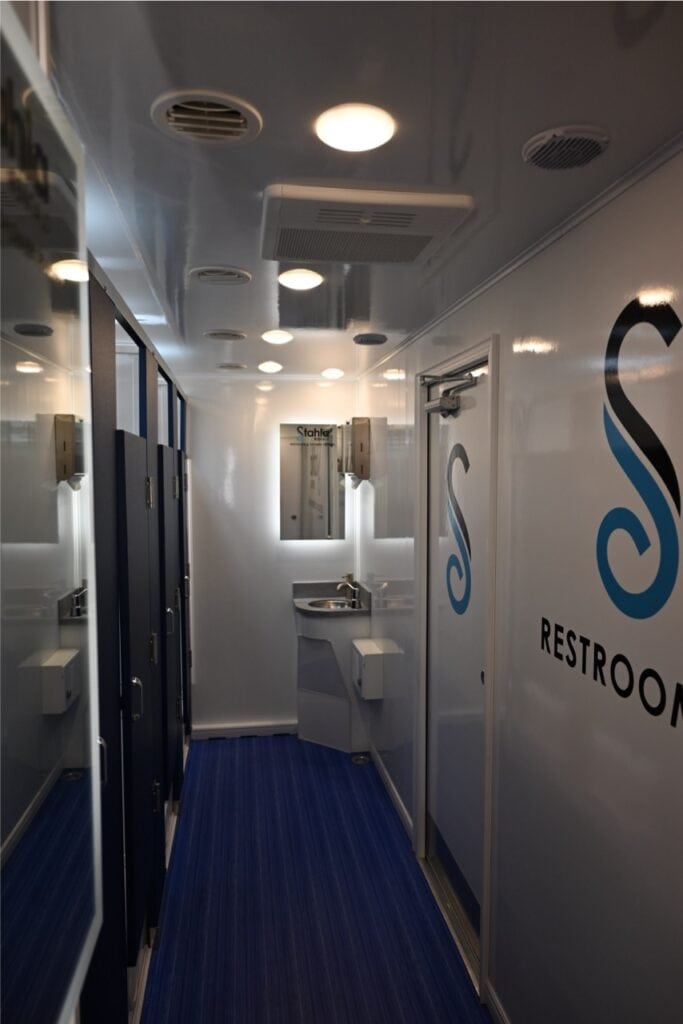 interior view of a clean, modern mobile shower unit with multiple stalls, blue flooring, white walls, and signage.