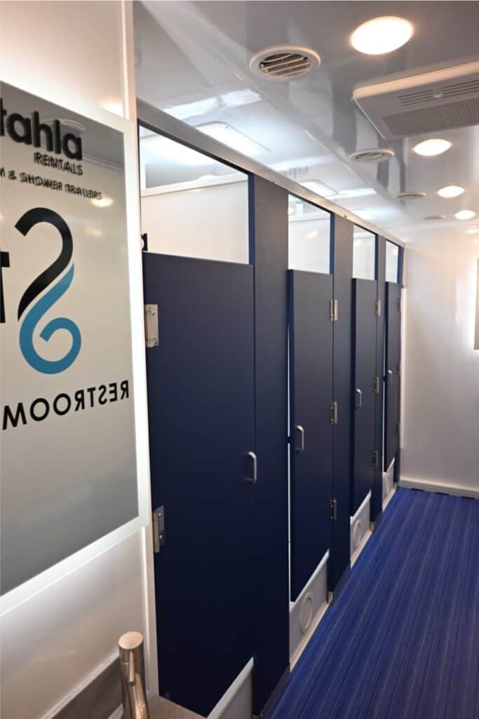 interior of a modern boat or ferry with a row of blue bathroom doors on one side, bright lighting, and an 8 station shower area.