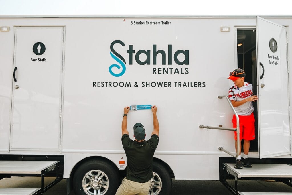 Men installing sign on restroom trailer rental.