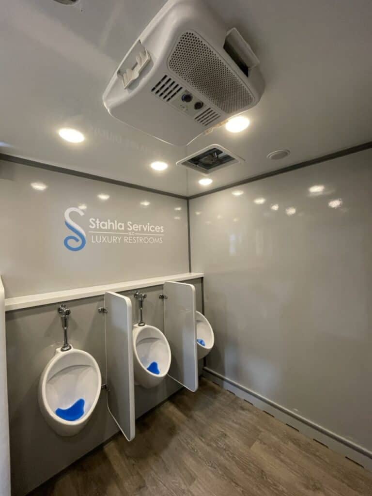 interior of a clean, modern 10 stall restroom trailer unit with three urinals featuring signage for "stahla services luxury restrooms.