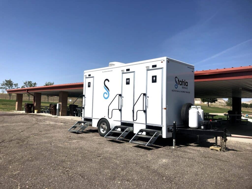 a 3 stall shower and restroom trailer is conveniently located on a paved area next to a covered picnic pavilion in a scenic park setting.