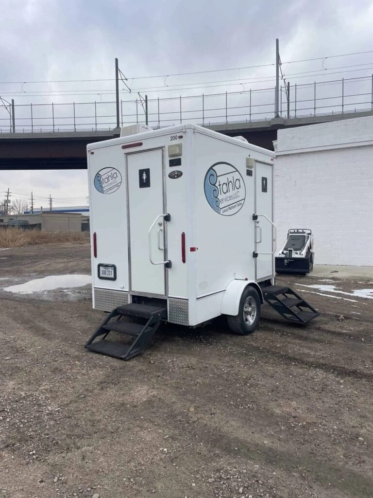 Mobile restroom trailer parked under overpass.