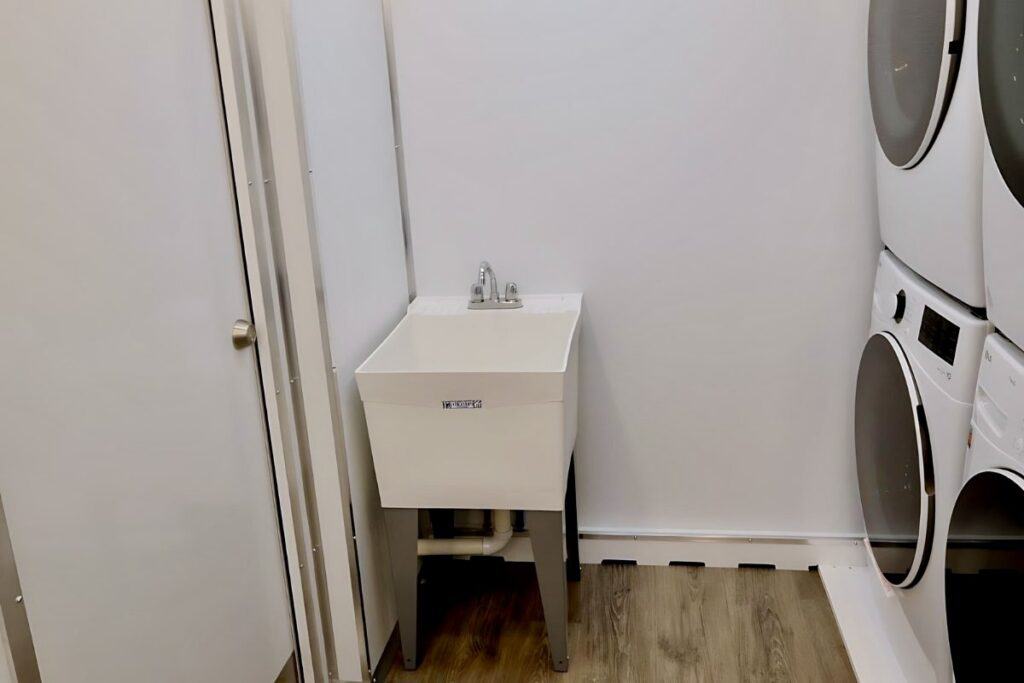 a laundry room with a white utility sink, washer, and dryer, featuring grey flooring and white walls.