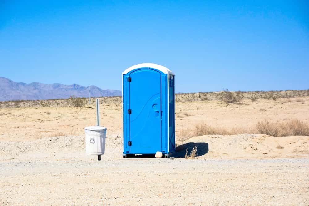 Portable toilet in desert landscape with trash can.
