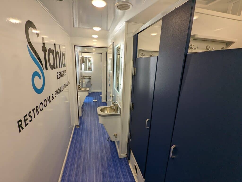 interior of a clean mobile shower unit facility with multiple closed blue doors, sinks, mirrors, and a sign reading "stahla rentals restroom solutions.