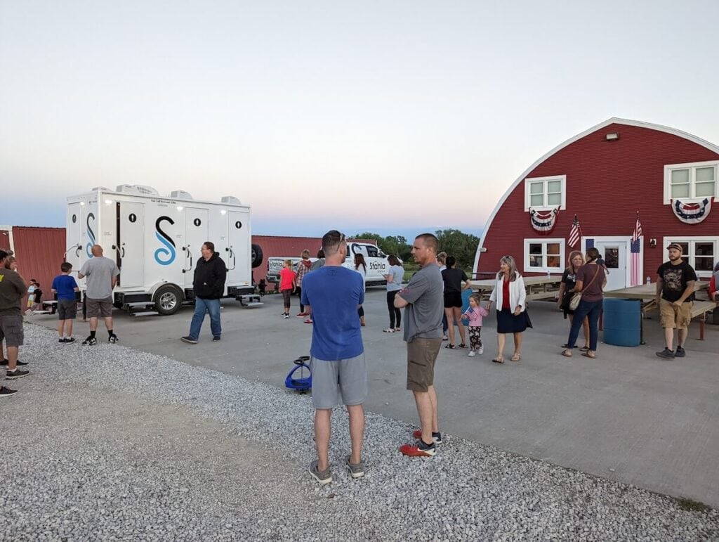 People gathered outside near mobile event trailer at dusk.