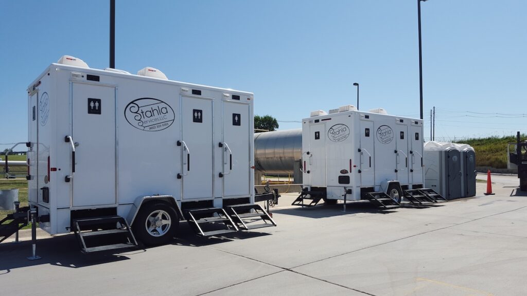 Mobile restroom trailers parked in sunny lot.